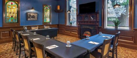 Un salón de conferencias con una larga mesa, sillas, una chimenea, vidrieras y una televisión.