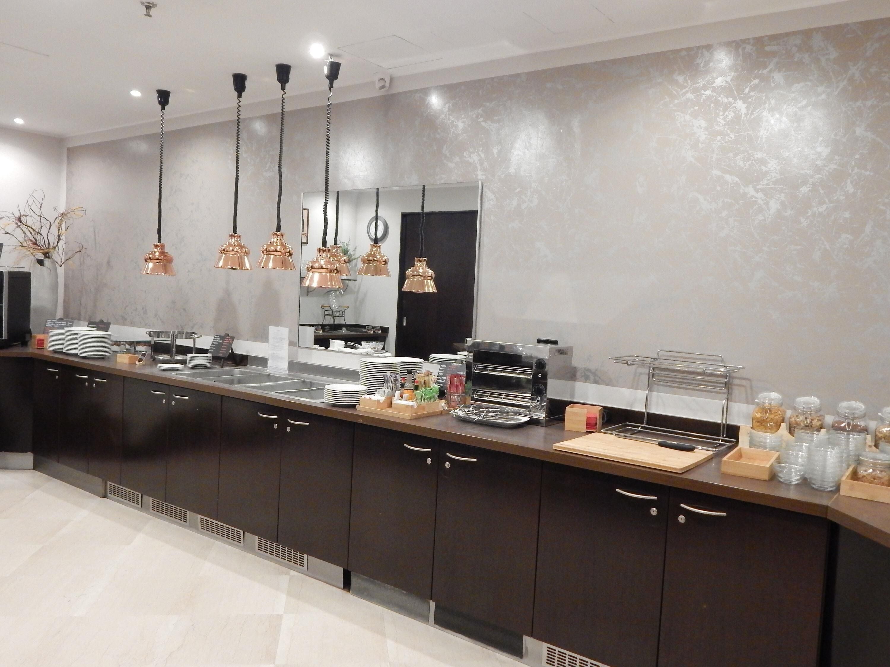 Una cucina moderna con mobili scuri, lampade a sospensione in rame, una macchina da caffè e un angolo buffet con piatti e posate.