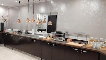 Una cucina moderna con mobili scuri, lampade a sospensione in rame, una macchina da caffè e un angolo buffet con piatti e posate.