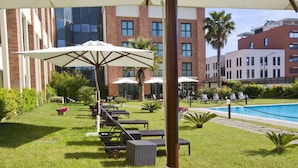 A poolside area with lounge chairs, umbrellas, and a swimming pool. - Mercure Rome Leonardo da Vinci Airport (Fiumicino)