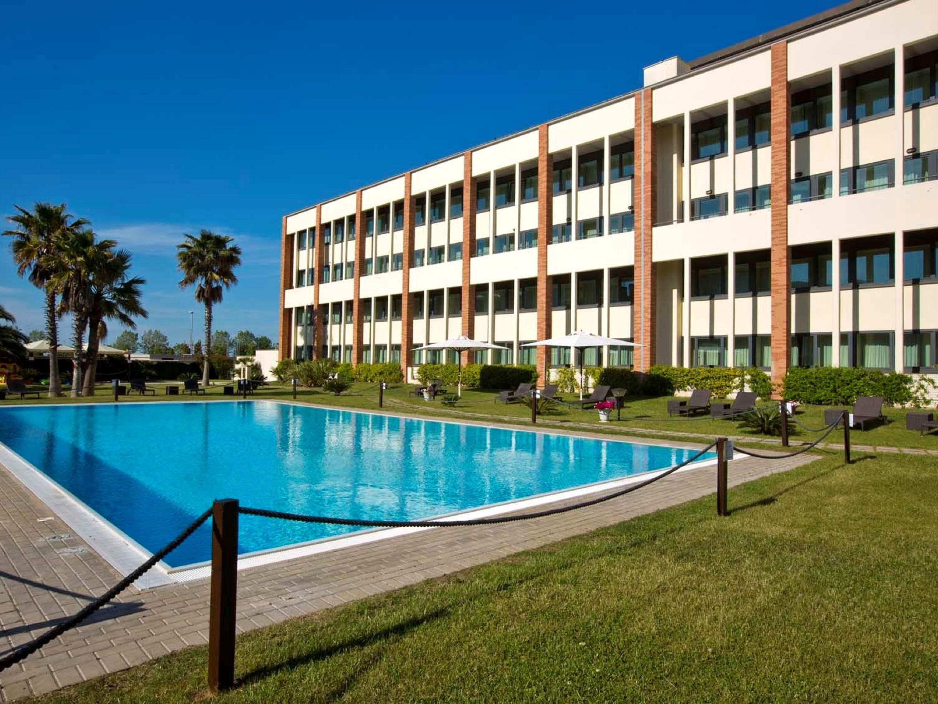 Ett modernt hotell med en swimmingpool, solstolar och palmer.
