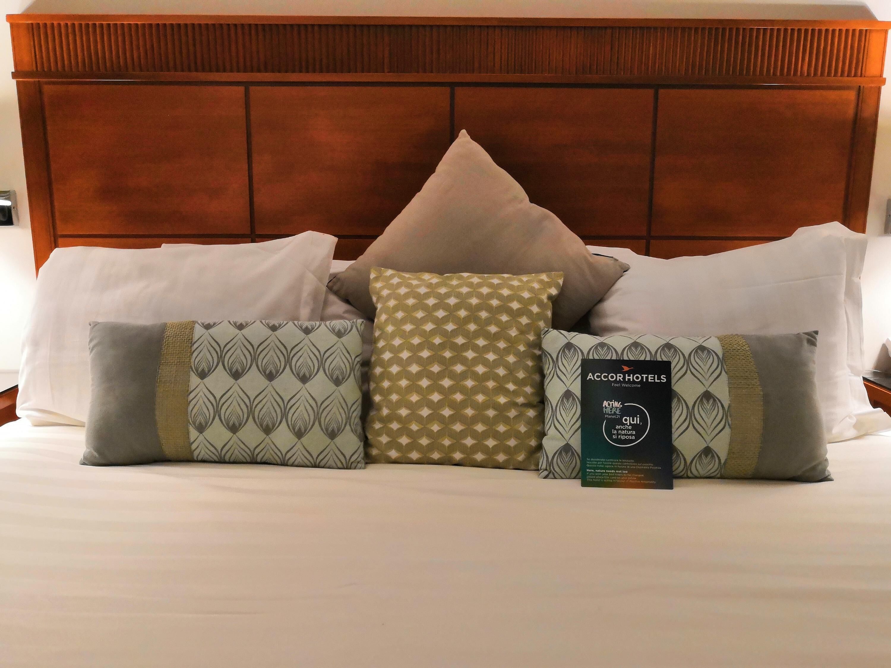 A hotel bed with a wooden headboard, multiple pillows, and a welcome booklet.