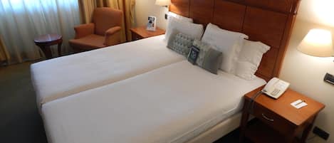 A hotel room with a double bed, two bedside tables, a lamp, a chair, and a window with curtains.
