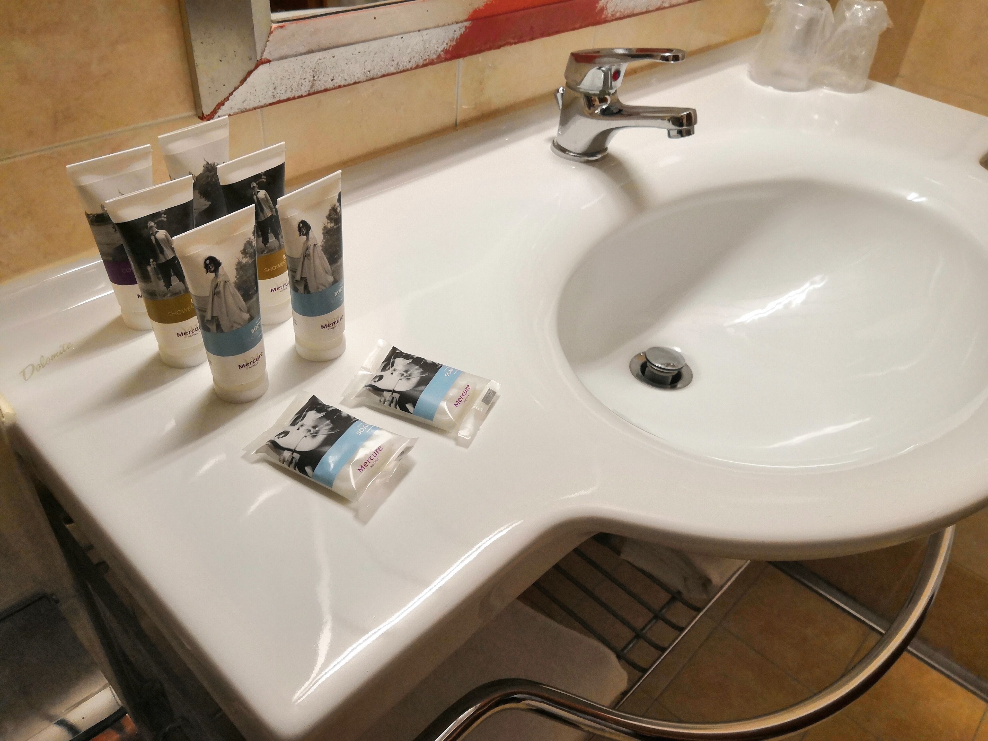 Un lavabo blanc avec un robinet chromé, un miroir et trois bouteilles de gel douche MeruCare sur le comptoir.