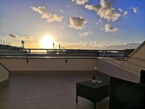 A balcony with a view of the sunset, a small table, and a chair. - Mercure Rome Leonardo da Vinci Airport (Fiumicino)