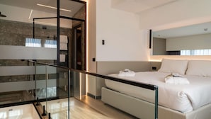 A modern hotel room with a glass railing, a bed with white linens, and a stone wall. - Mercure Rome Leonardo da Vinci Airport (Fiumicino)