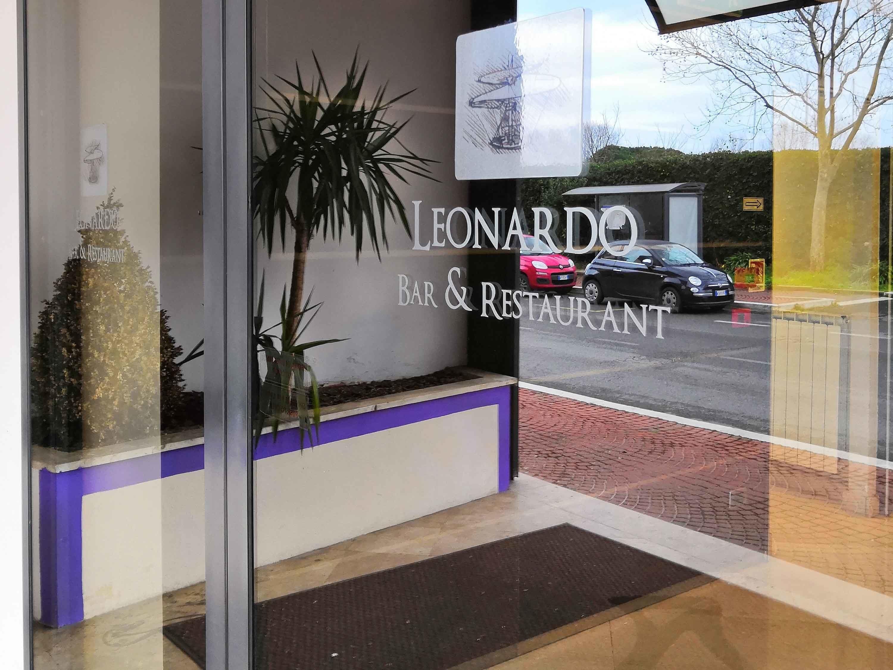 A storefront with 'LEONARDO BAR & RESTAURANT' signage, a potted plant, and a reflection of a car and trees.
