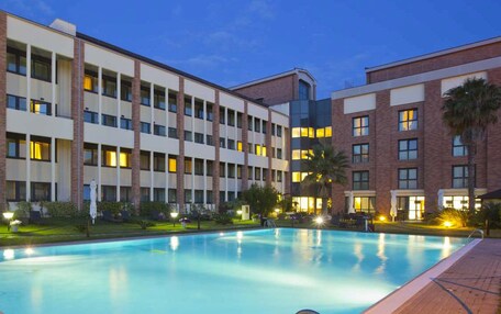 A hotel with a swimming pool, multiple floors, and a well-lit exterior.
