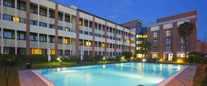 A hotel with a swimming pool, multiple floors, and a well-lit exterior. - Mercure Rome Leonardo da Vinci Airport (Fiumicino)