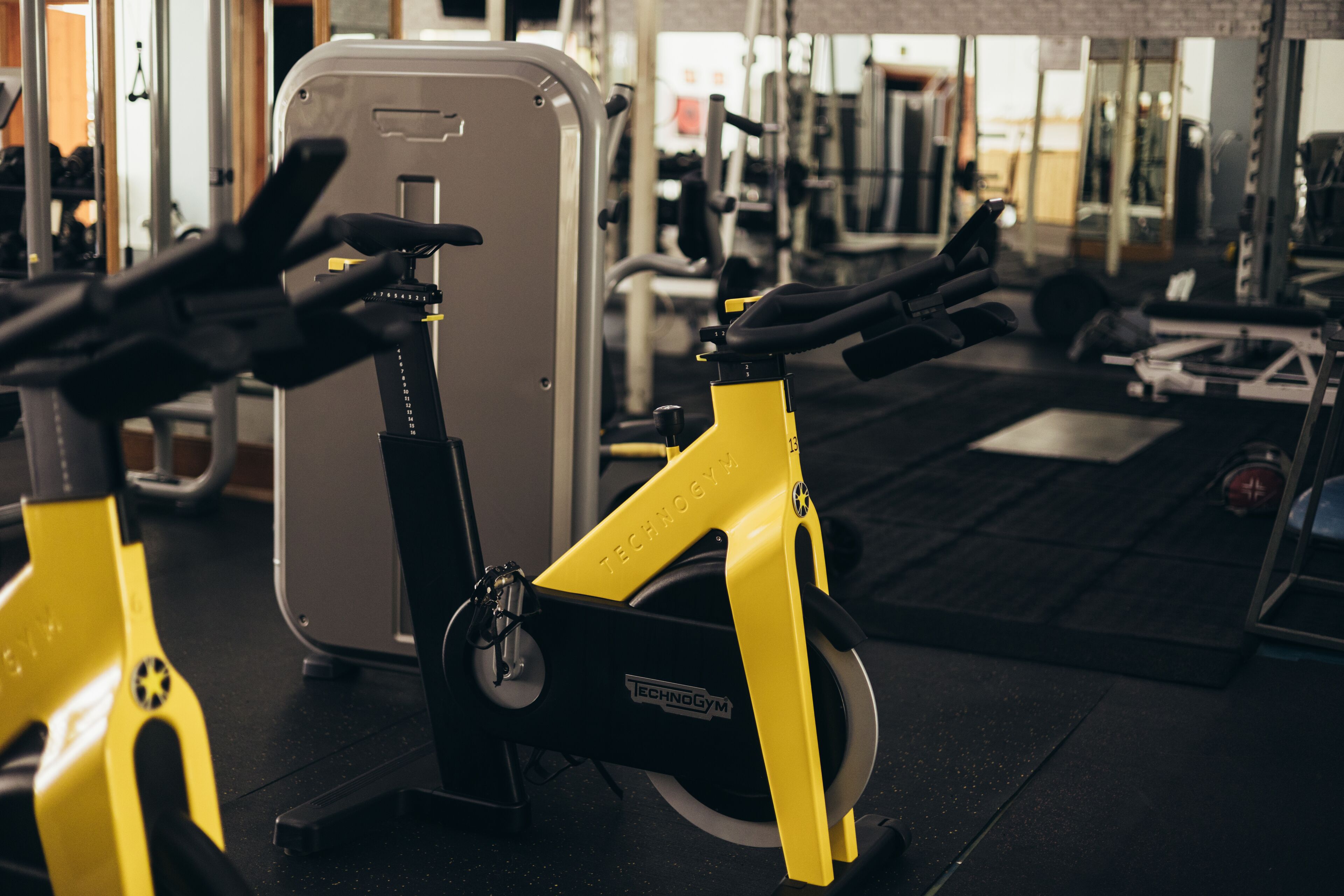 A stationary bike in a gym with a mirror and various exercise equipment in the background.