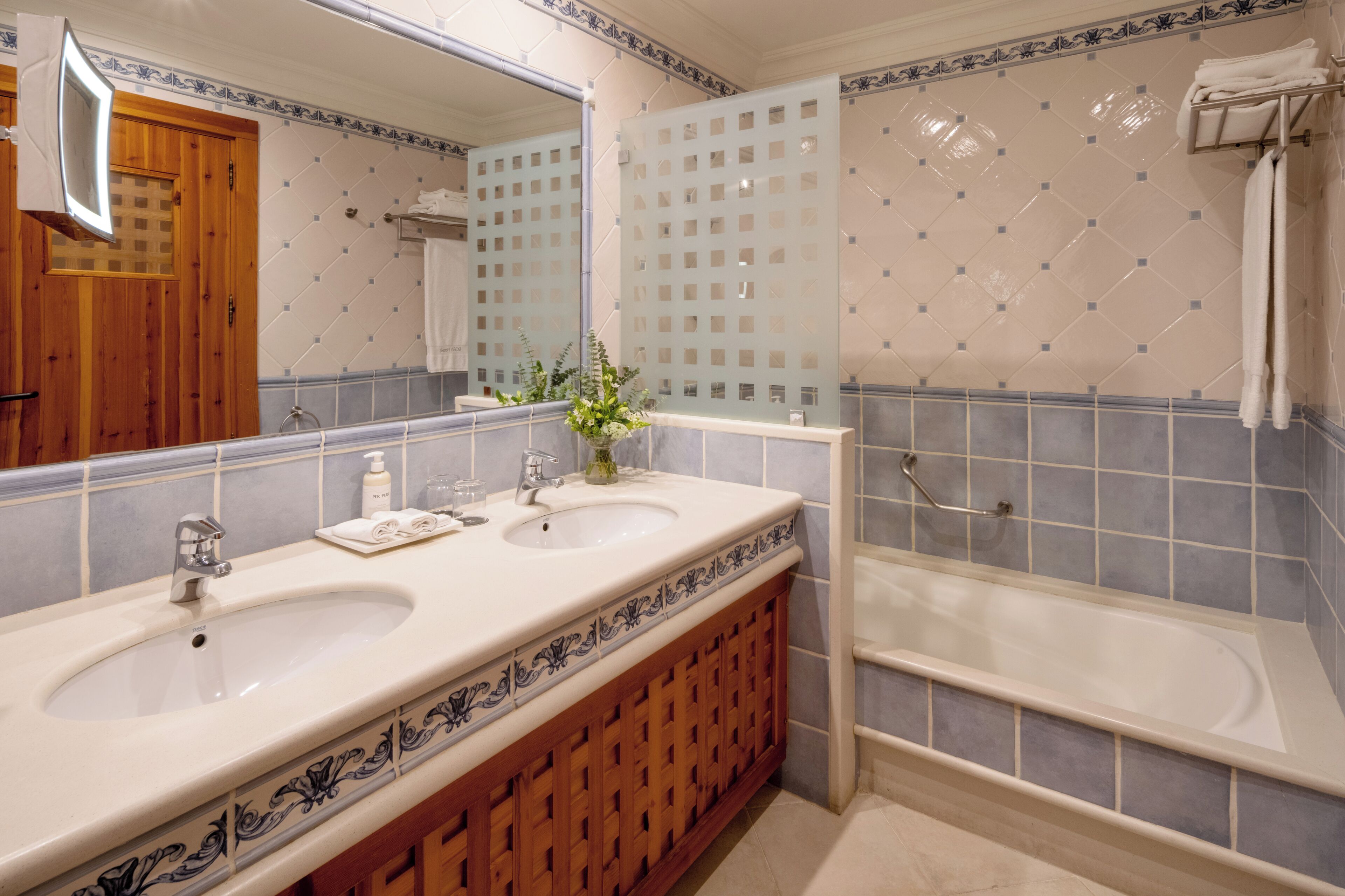 A bathroom with two sinks, a mirror, a bathtub, and a wooden cabinet.