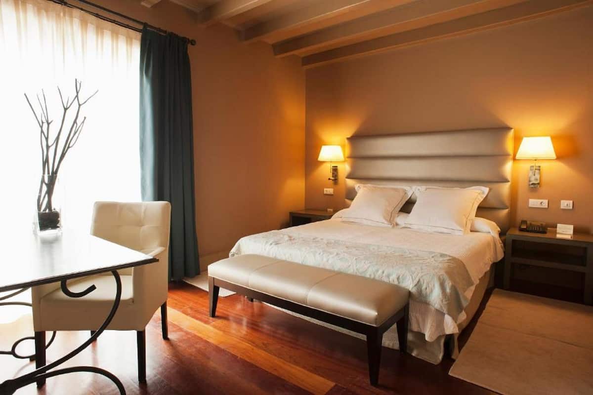 Ein Hotelzimmer mit Bett, Nachttischlampen, einer Bank, einem Tisch und einem Stuhl.