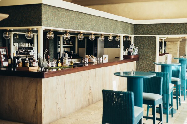 Un espace bar doté d’un comptoir en marbre, de nombreuses bouteilles et de chaises de couleur turquoise.