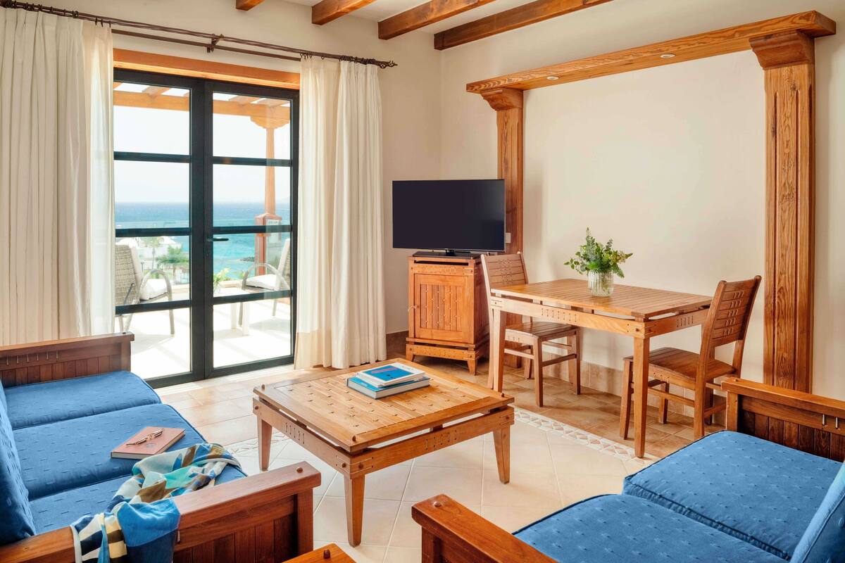 Ein gemütliches Wohnzimmer mit großem Fenster, Holzmöbeln, einem Flachbildfernseher und einem Essbereich.