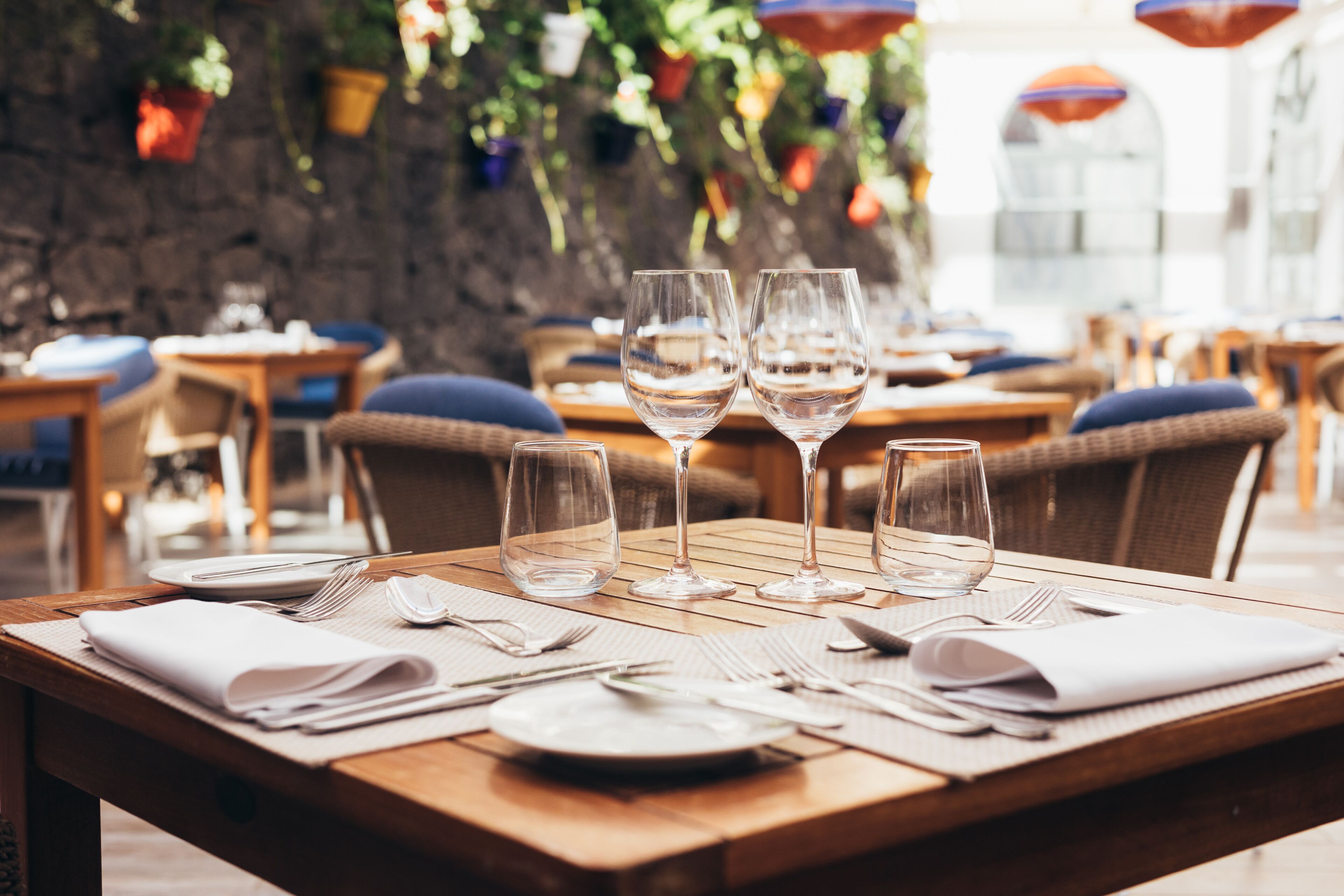 A restaurant table set with white plates, cutlery, and three clear wine glasses.