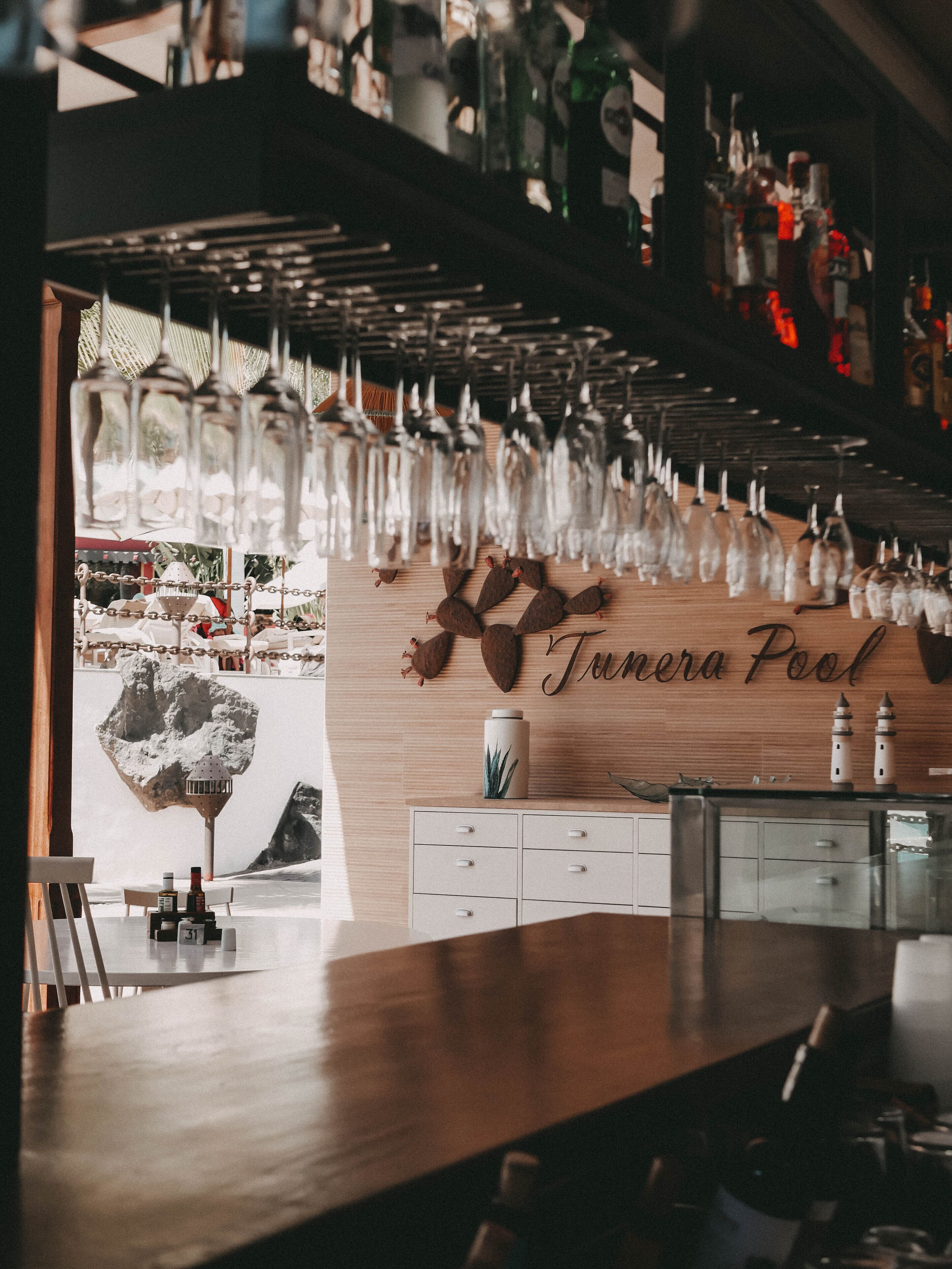 Una zona de bar con mostrador de madera, copas de vino colgando y una pared con la inscripción "Tamera Pool".