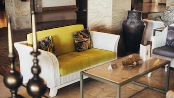 A lobby with a white wicker sofa with a green cushion, a glass coffee table, and a large vase.