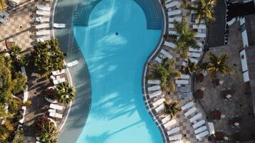 Vista aérea de un resort con una gran piscina rodeada de sillas de descanso y palmeras.
