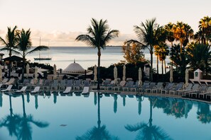 Ein Poolbereich mit Liegestühlen und Sonnenschirmen, Palmen und Blick auf den Ozean.