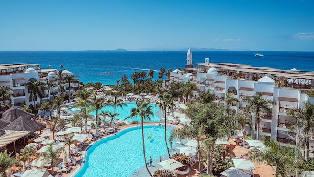 A resort with a large pool, palm trees, and a view of the ocean. - Princesa Yaiza Suite Hotel Resort (Yaiza)