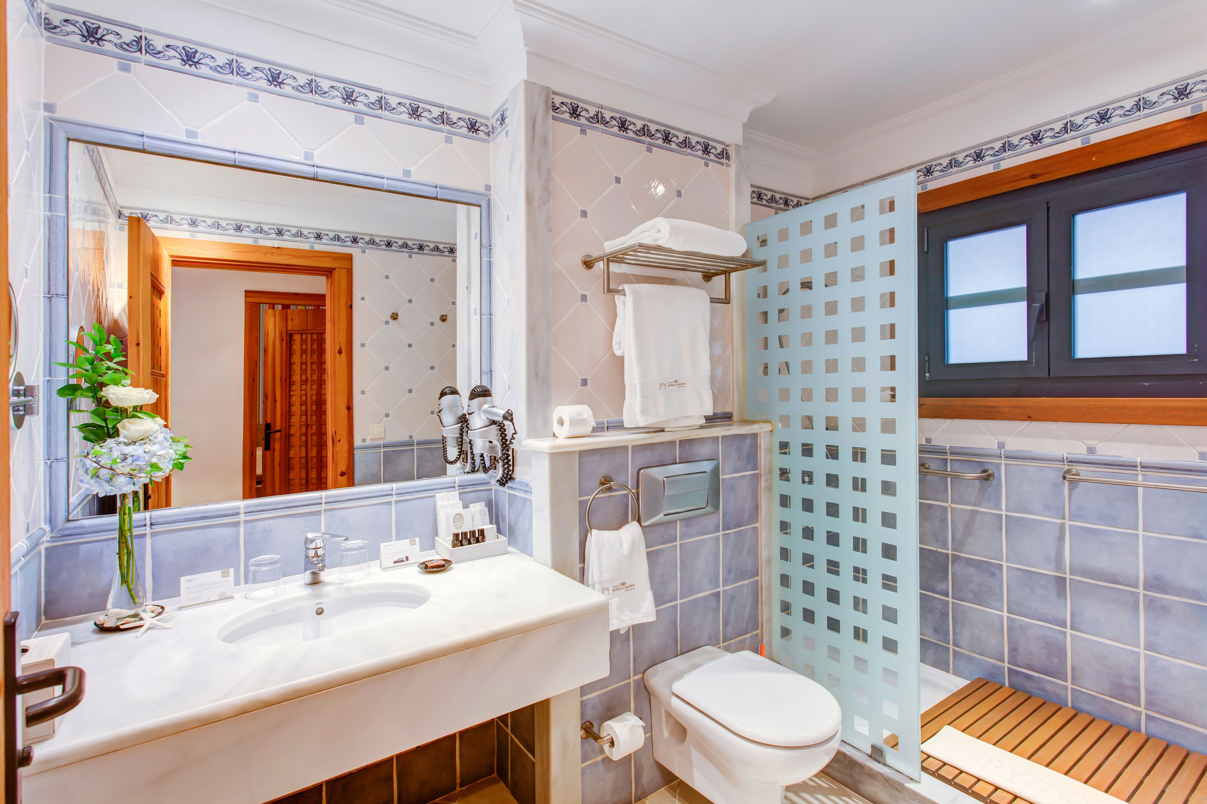 Un baño con un espejo grande, un lavamanos con artículos de aseo, un inodoro y una zona de ducha.