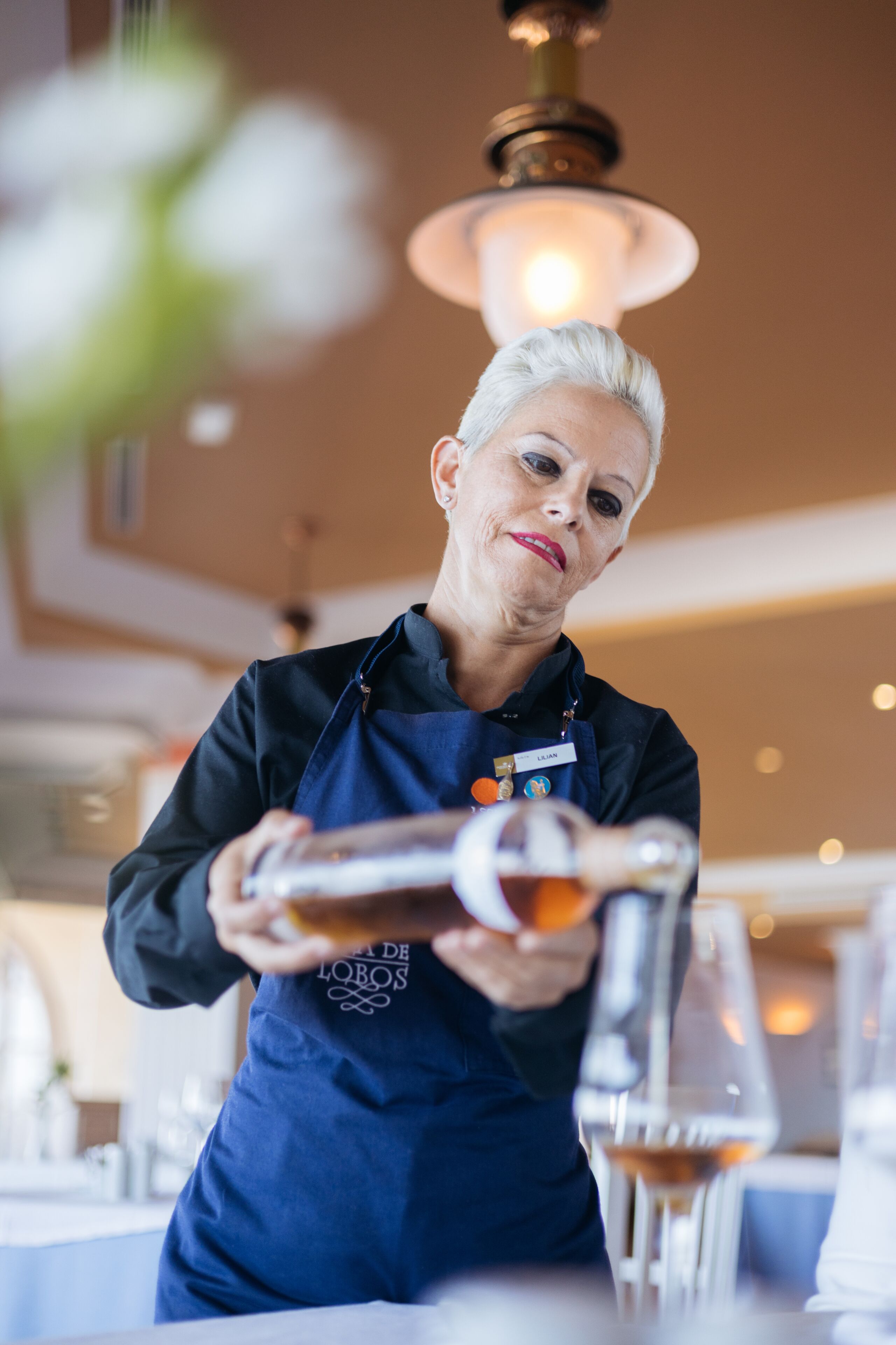 Une personne portant un tablier bleu verse une boisson dans un verre.