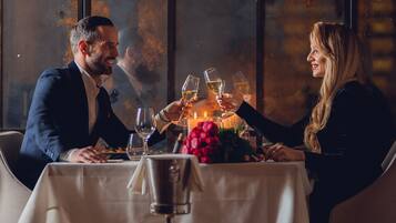 A couple dining at a table with a candle centerpiece, in a dimly lit room with large windows.