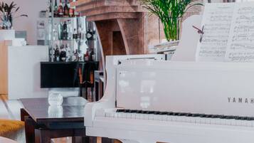 A piano in a modern living room with a dining area, a bookshelf, and a plant.