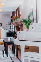 A piano in a modern living room with a dining area, a bookshelf, and a plant.