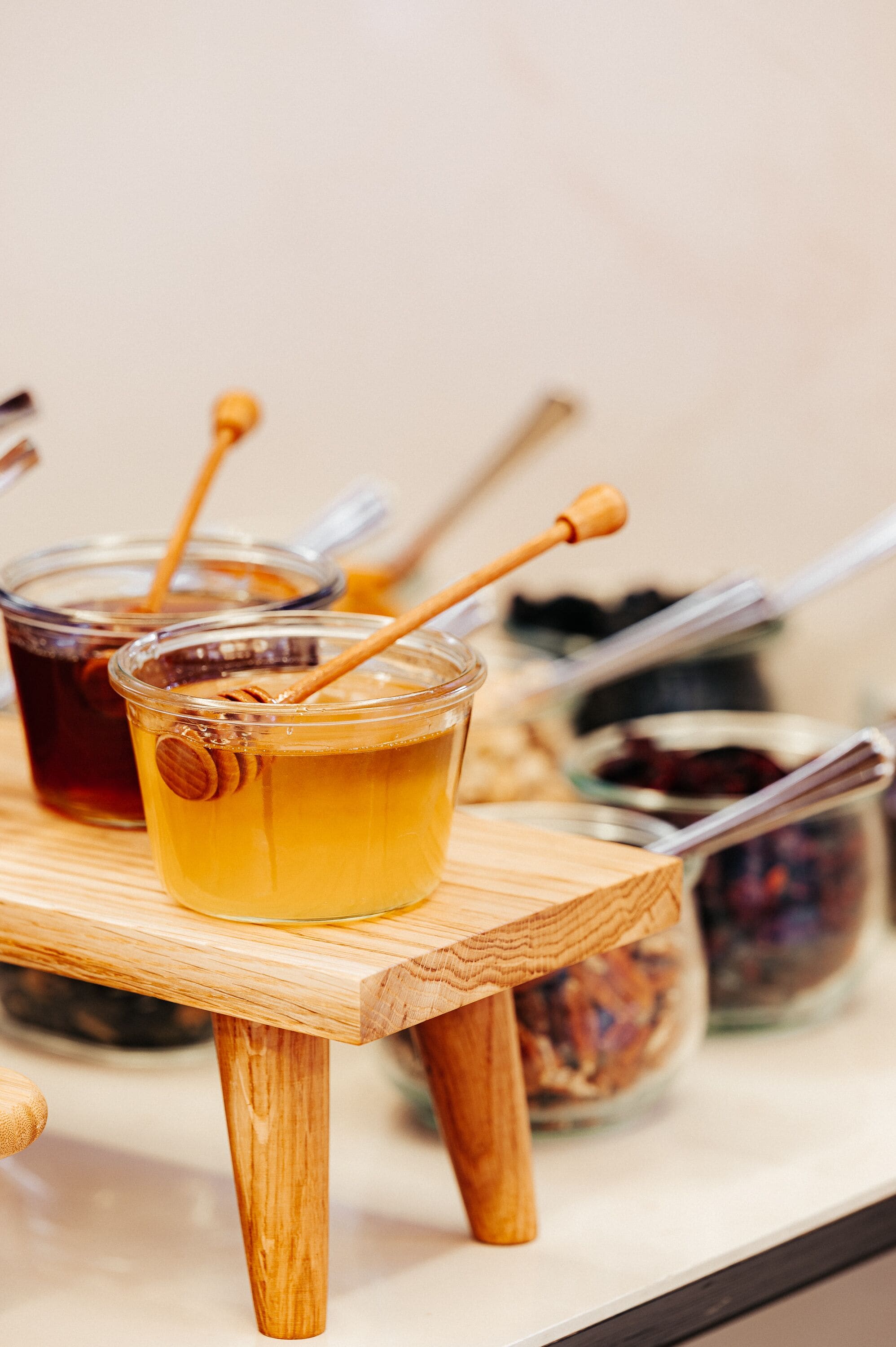 Two glasses of honey on a wooden table with honey dipper utensils.