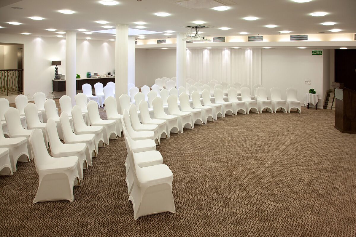 A conference room with rows of white chairs, a carpeted floor, and a stage with a podium.