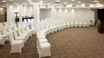 A conference room with rows of white chairs, a carpeted floor, and a stage with a podium.