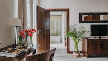 Hotellihuone, jossa on puinen työpöytä, televisio, ruukussa oleva kasvi ja näkymä kylpyhuoneeseen.