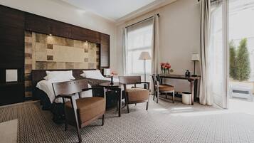 A hotel room with a bed, a desk, two chairs, a lamp, and a view of the outdoors.