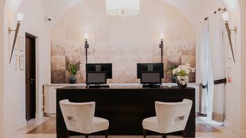 A reception area with a marble wall, two reception desks, a chandelier, and two chairs.