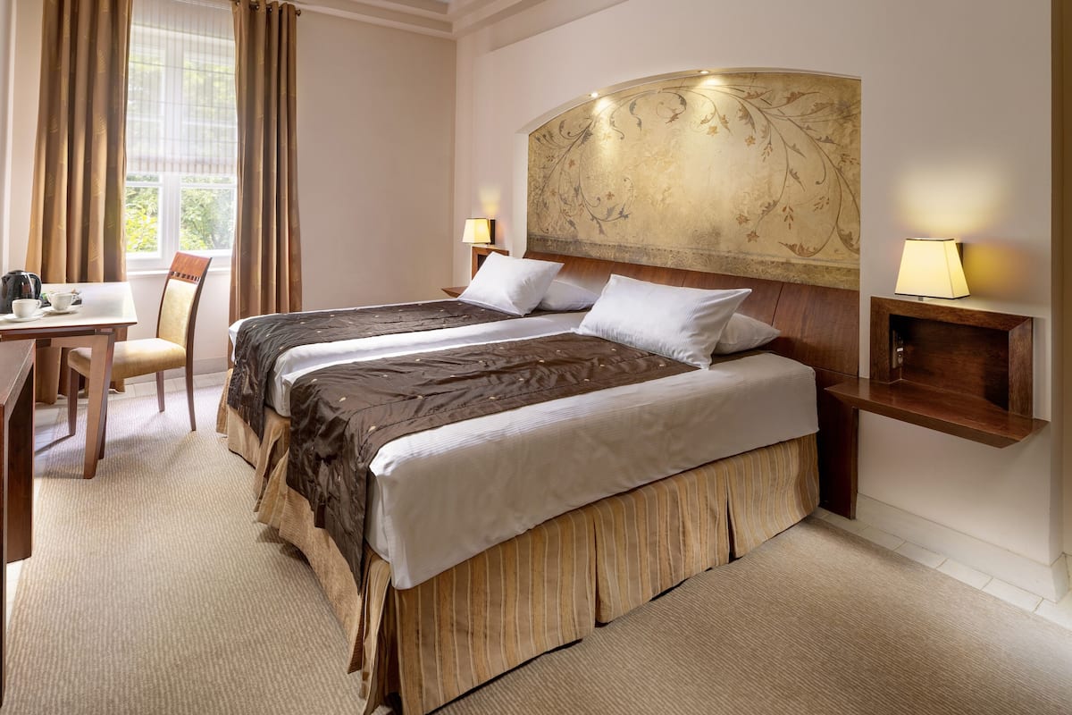 Une chambre d’hôtel avec un grand lit, deux tables de chevet avec des lampes, un bureau avec une chaise et une fenêtre avec des rideaux.