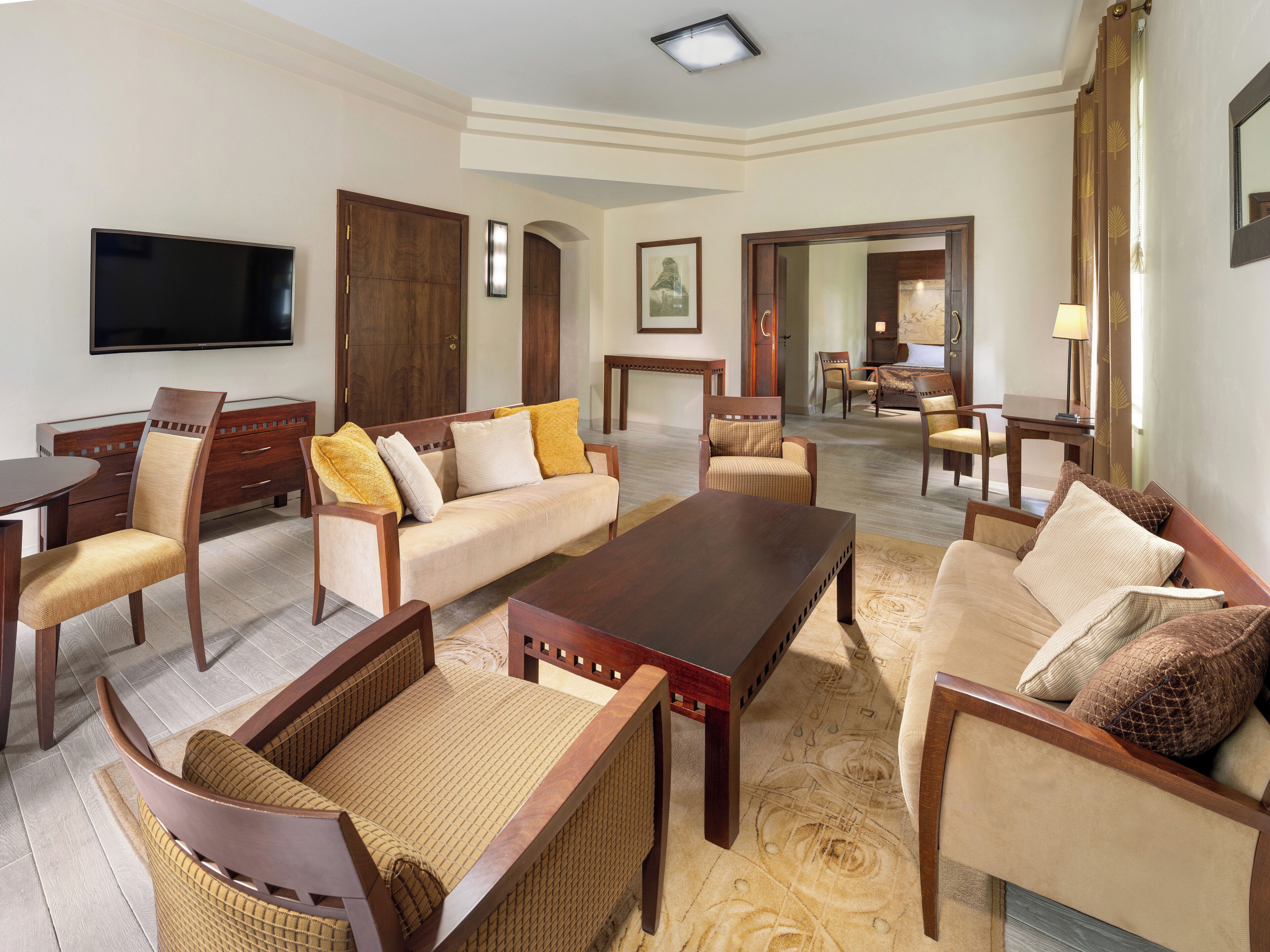A spacious living room with a sofa, armchairs, a coffee table, and a TV mounted on the wall.