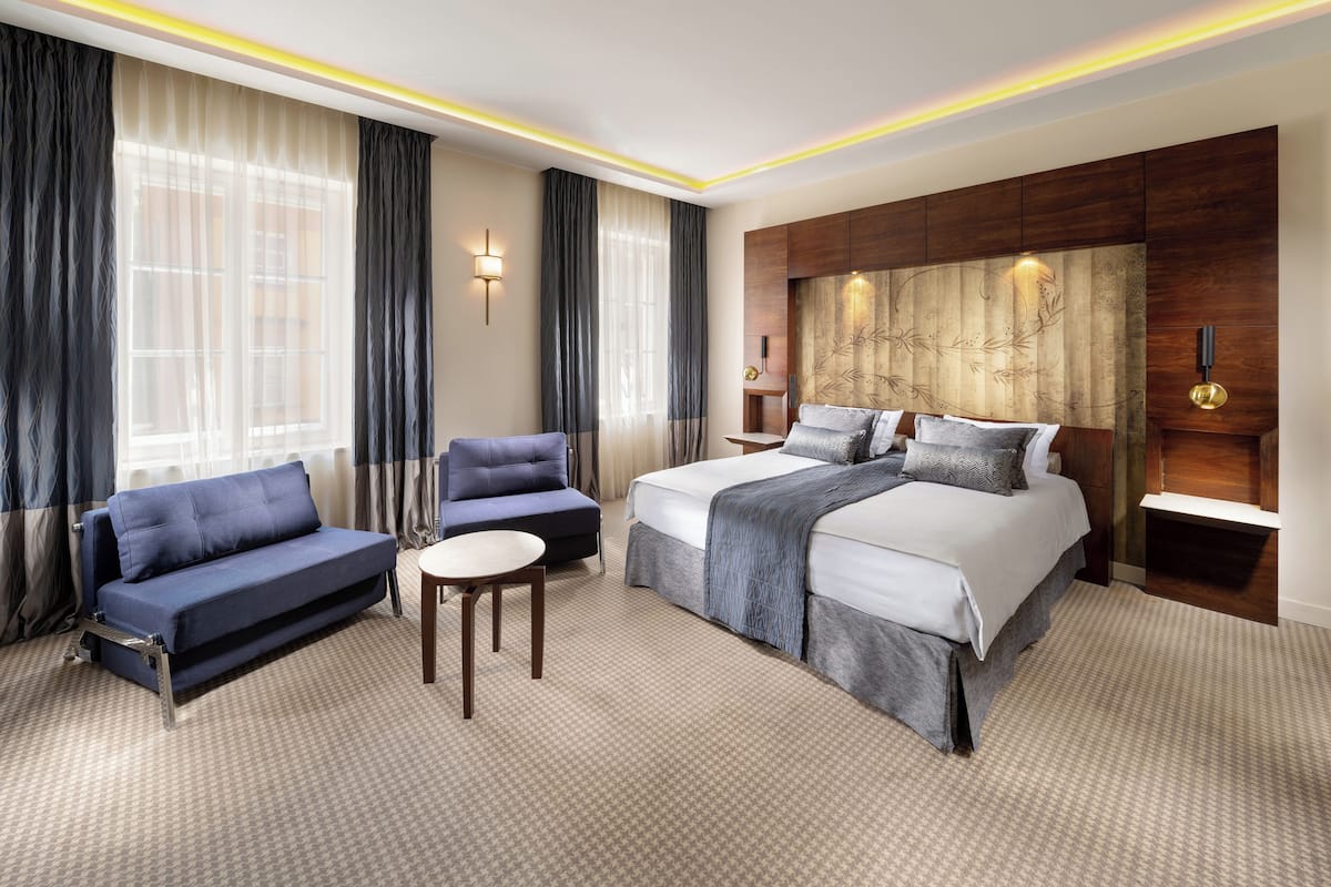 Une chambre d’hôtel moderne avec un grand lit, un canapé, une petite table et un panneau décoratif au mur.