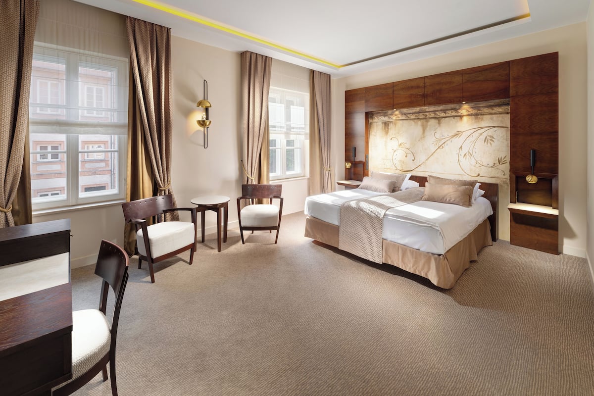 Une chambre d’hôtel spacieuse, dotée d’un grand lit, de deux fauteuils, d’une petite table et d’un bureau.