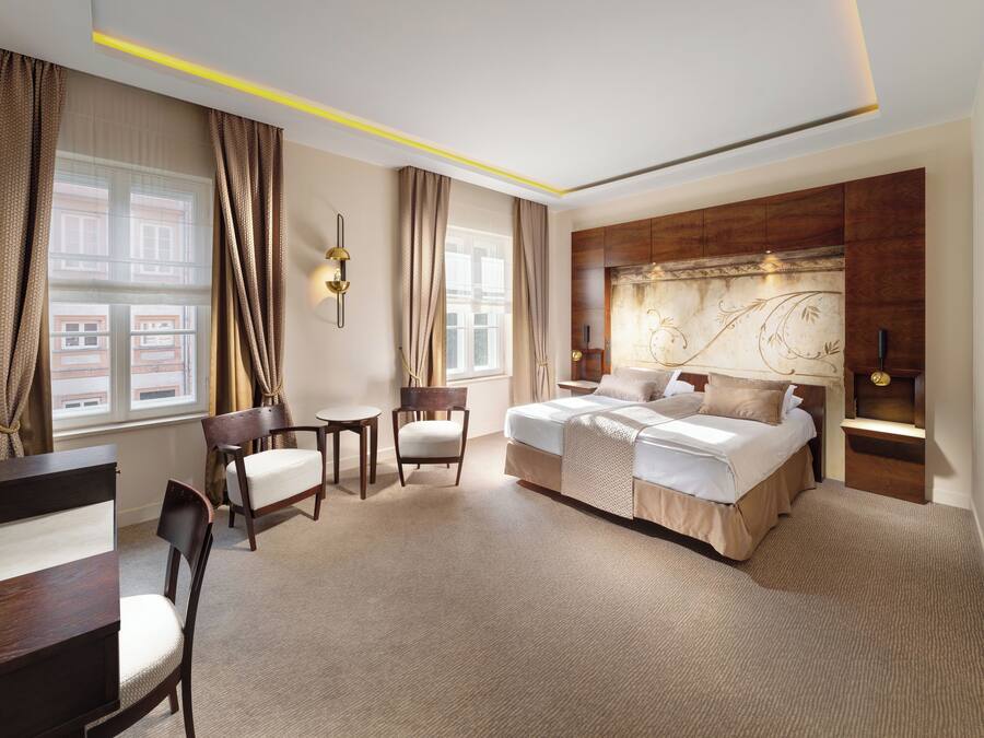 A spacious hotel room with a large bed, two chairs, a small table, and a desk.