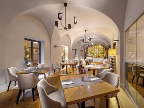 Een ruime eethoek met hoge gewelfde plafonds en een centrale bar. Tafels zijn klaar voor gebruik met stoelen, en een kroonluchter hangt aan het plafond.