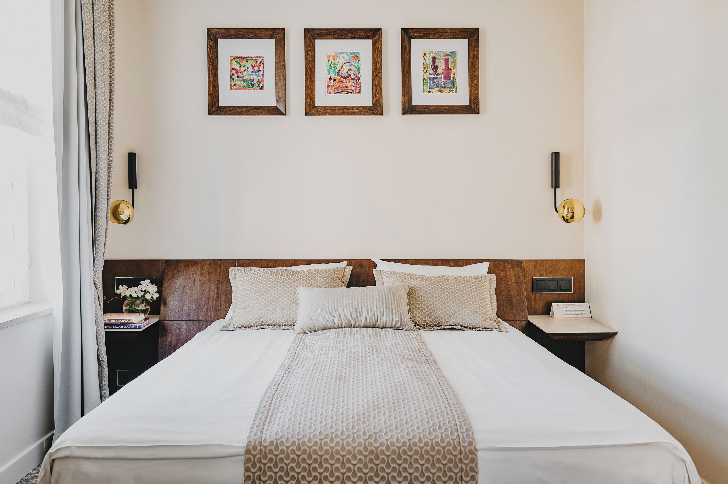 A neatly made bed with a patterned bedspread, a wooden headboard, and three framed artworks on the wall.