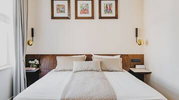 A neatly made bed with a patterned bedspread, a wooden headboard, and three framed artworks on the wall.