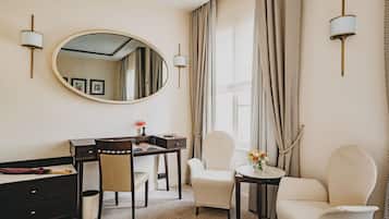 Een hotelkamer met een bureau, twee stoelen, een ronde spiegel en een raam met gordijnen.