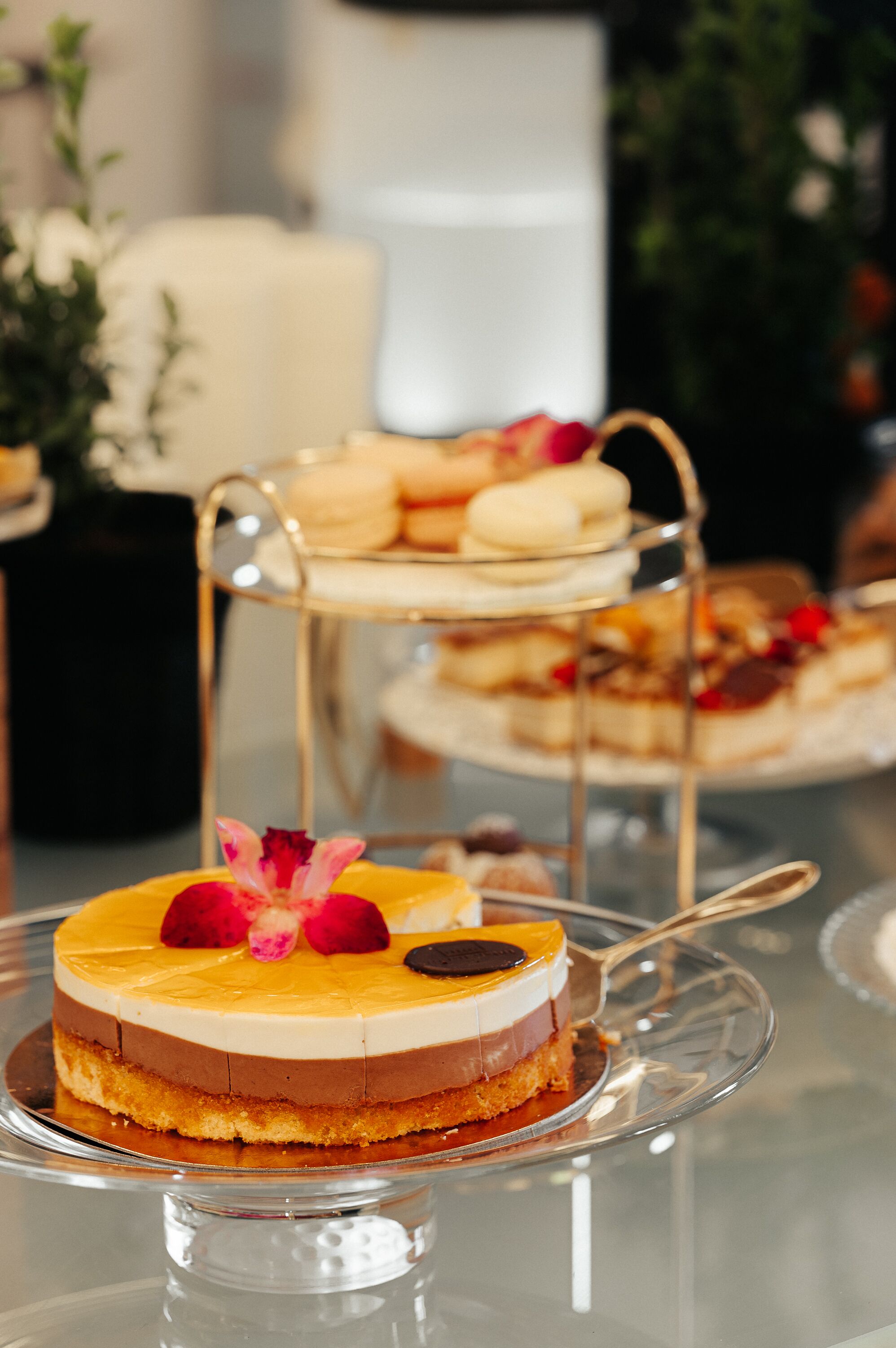 Una exposición de postres con un pastel en capas y macarons sobre un soporte de vidrio.