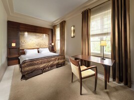 Ein Hotelzimmer mit einem großen Bett, einem Schreibtisch, einem Stuhl und einem Fenster mit Vorhängen.