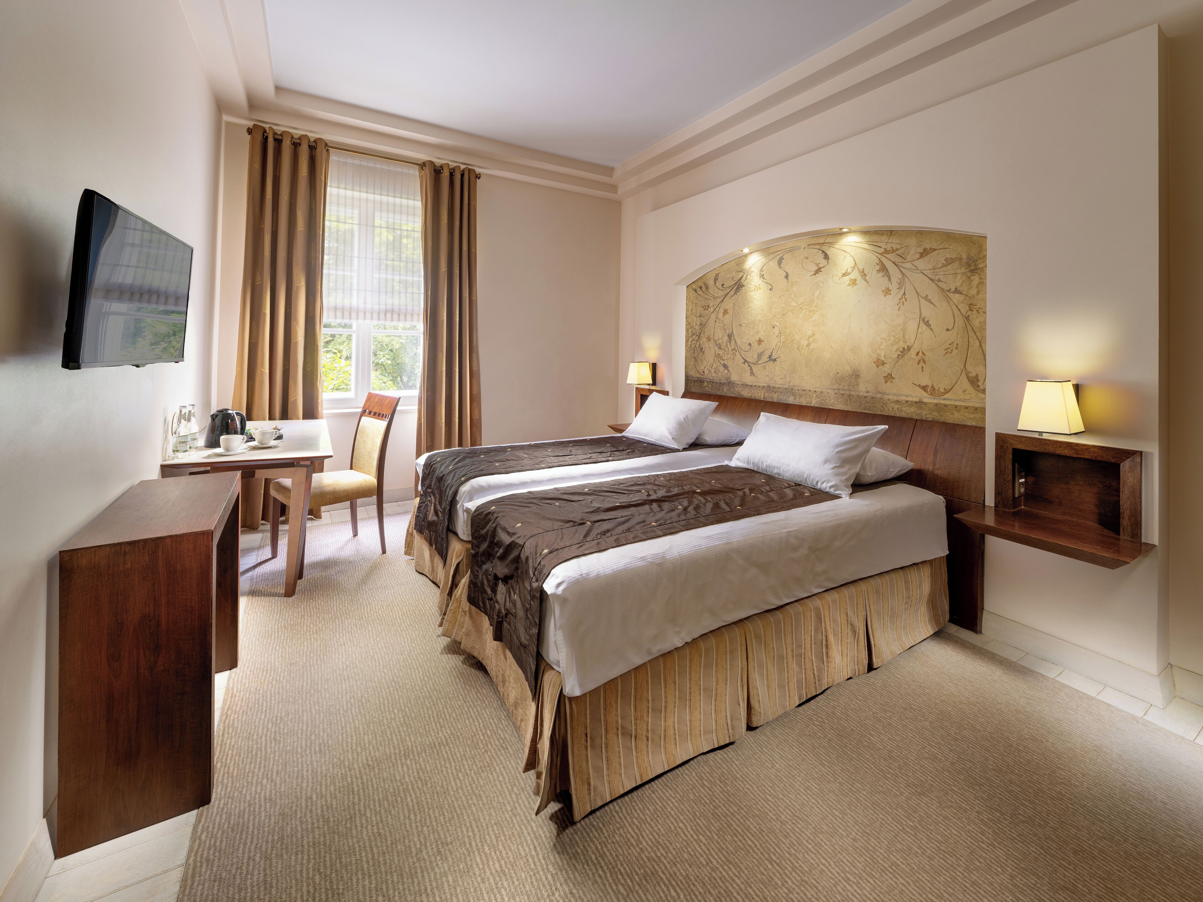 Hotelkamer met een bed, nachtkastje, stoel, bureau, televisie en raam met gordijnen.