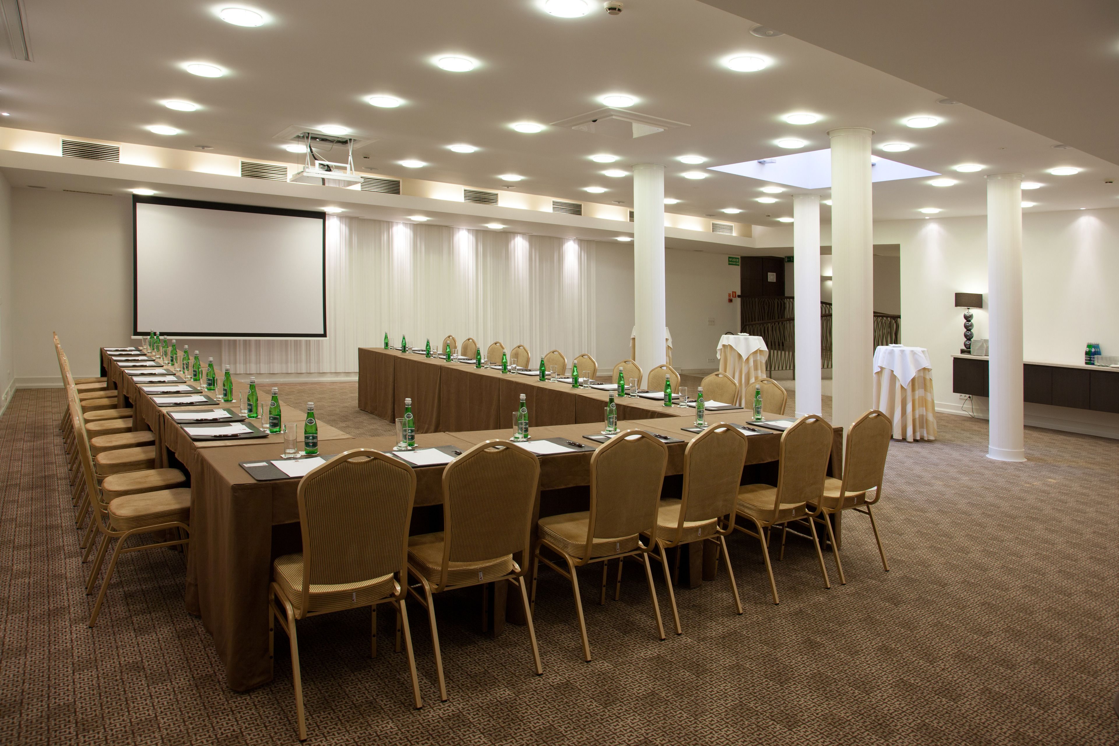 A conference room with a long table, chairs, a projector screen, and a carpeted floor.