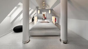 Een moderne loft slaapkamer met dakraam, een groot bed en een opvallende kolomstructuur.