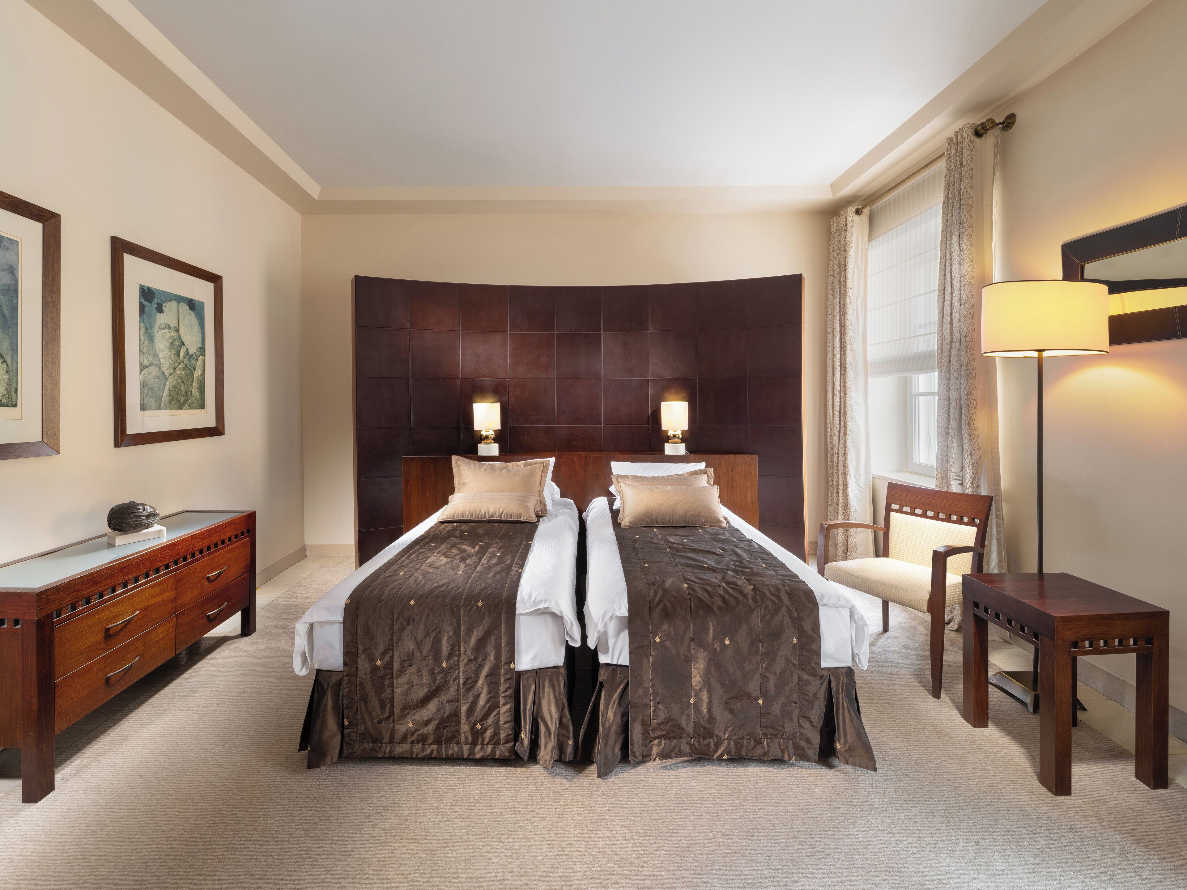 Habitación de hotel con dos camas, un escritorio, una silla y un ventanal con cortinas.